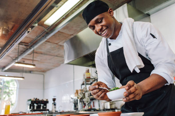 Gourmet chef in uniform cooking in a commercial kitchen. Happy male cook wearing apron standing by kitchen counter preparing food.